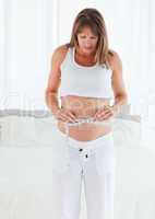 Good looking pregnant female using a tape measure while standing