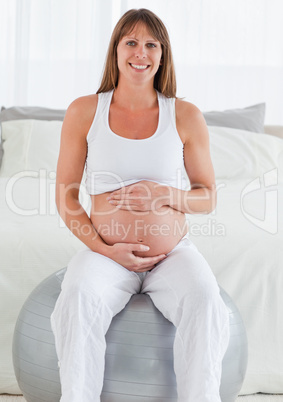 Charming pregnant female caressing her belly while sitting on a