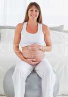 Charming pregnant female caressing her belly while sitting on a