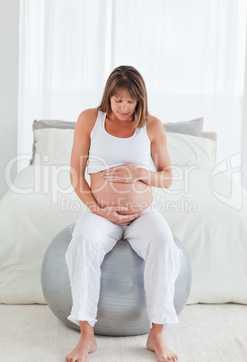 Lovely pregnant female caressing her belly while sitting on a gy