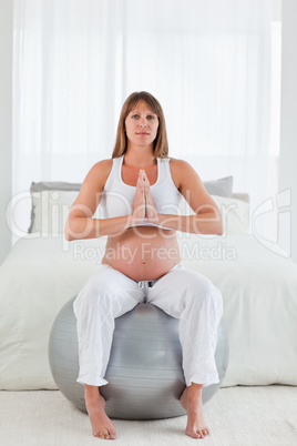 Charming pregnant female doing relaxation exercises while sittin