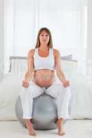 Beautiful pregnant female doing relaxation exercises while sitti
