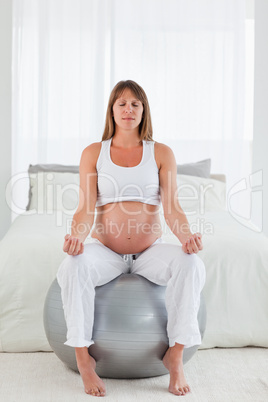 Attractive pregnant female doing relaxation exercises while sitt