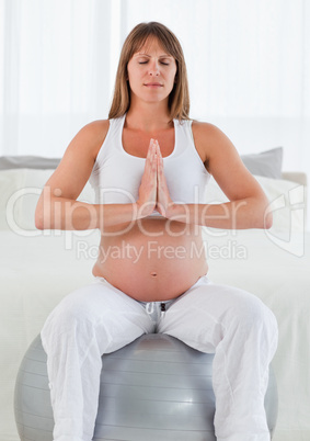 Lovely pregnant female doing relaxation exercises while sitting