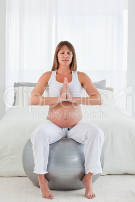 Good looking pregnant female doing relaxation exercises while si