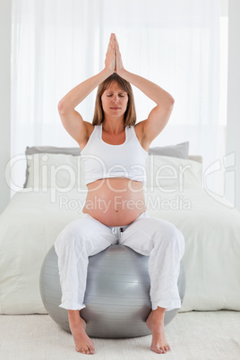 Pretty pregnant female doing relaxation exercises while sitting