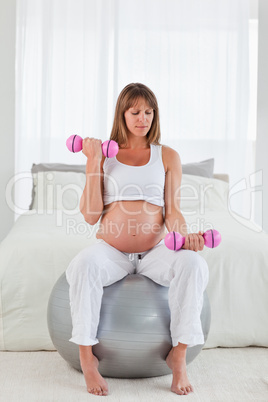 Beautiful pregnant female using a dumbbell while sitting on a gy