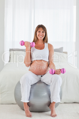 Attractive pregnant female using a dumbbell while sitting on a g