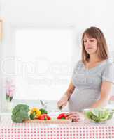 Pretty pregnant woman posing while cooking vegetables