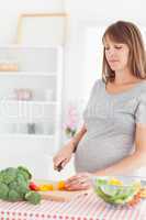 Charming pregnant woman posing while cooking vegetables