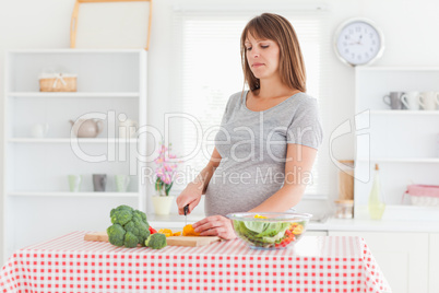 Lovely pregnant woman posing while cooking vegetables