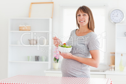 Lovely pregnant woman eating a cherry tomato while standing