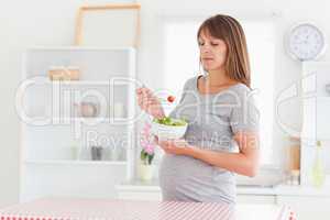 Beautiful pregnant woman eating a cherry tomato while standing