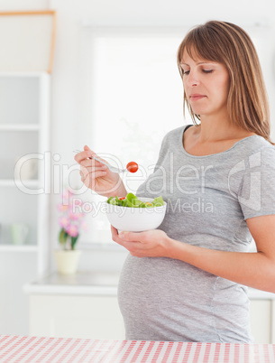 Good looking pregnant woman eating a cherry tomato while standin