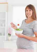 Charming pregnant woman eating a cherry tomato while standing