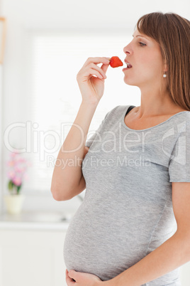 Pretty pregnant woman eating a strawberry while standing