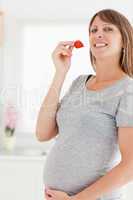 Beautiful pregnant woman eating a strawberry while standing