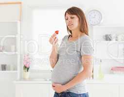 Good looking pregnant woman eating a strawberry while standing