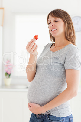 Attractive pregnant woman eating a strawberry while standing