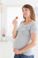 Attractive pregnant woman eating a strawberry while standing