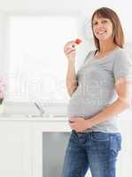 Lovely pregnant woman eating a strawberry while standing