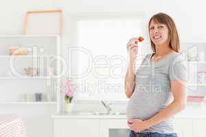 Charming pregnant woman eating a strawberry while standing