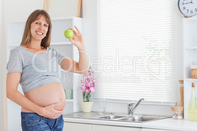 Beautiful pregnant woman posing while holding a green apple