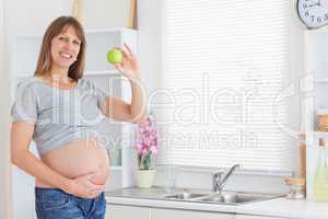 Beautiful pregnant woman posing while holding a green apple