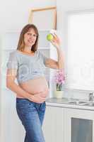Attractive pregnant woman posing while holding a green apple