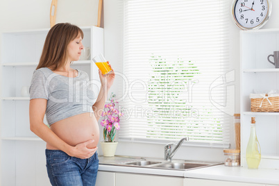 Beautiful pregnant woman drinking a glass of orange juice while