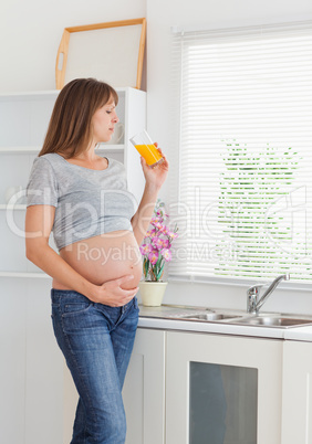 Attractive pregnant woman drinking a glass of orange juice while