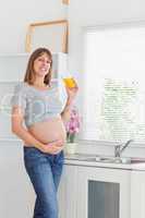 Beautiful pregnant woman holding a glass of orange juice while s