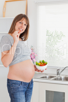 Lovely pregnant woman eating vegetables while standing