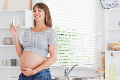 Pretty pregnant woman holding a glass of water while standing