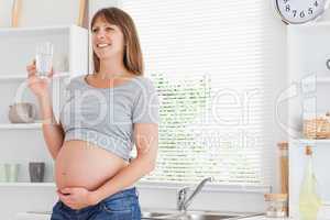 Pretty pregnant woman holding a glass of water while standing