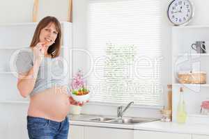Beautiful pregnant woman eating vegetables while standing