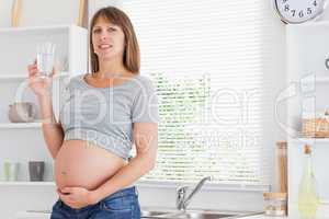 Beautiful pregnant woman holding a glass of water while standing