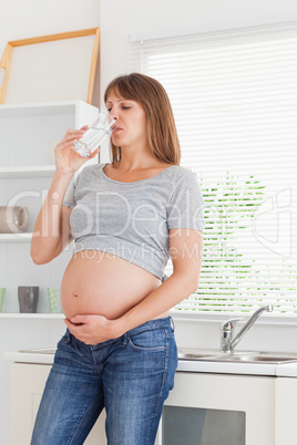 Good looking pregnant woman holding a glass of water while stand