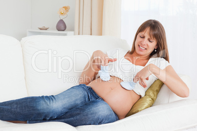 Beautiful pregnant woman playing with baby shoes while lying