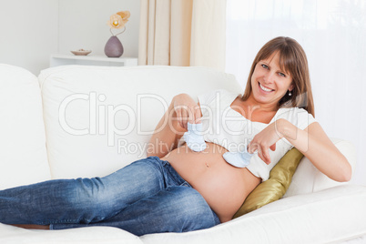 Attractive pregnant woman playing with baby shoes while lying