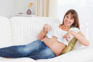 Attractive pregnant woman playing with baby shoes while lying