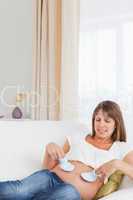 Good looking pregnant woman playing with baby shoes while lying