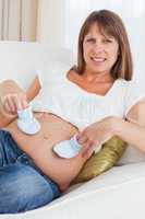 Pretty pregnant woman playing with baby shoes while lying
