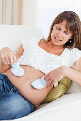 Charming pregnant woman playing with baby shoes while lying