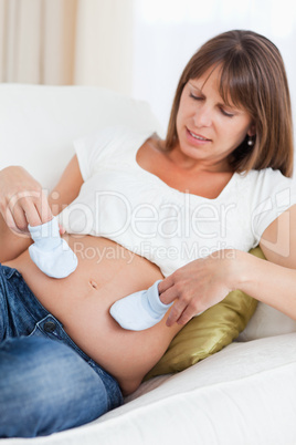 Beautiful pregnant woman playing with baby shoes while lying