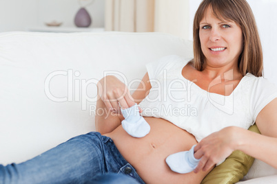 Young pregnant woman playing with baby shoes while lying