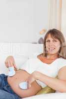 Cute pregnant woman playing with baby shoes while lying
