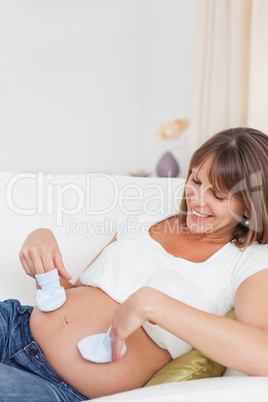 Pregnant woman playing with baby shoes while lying