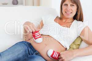 Good looking pregnant female playing with red baby shoes while l