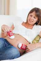 Gorgeous pregnant female playing with red baby shoes while lying